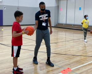 African American man assisting a boy holding basketball.